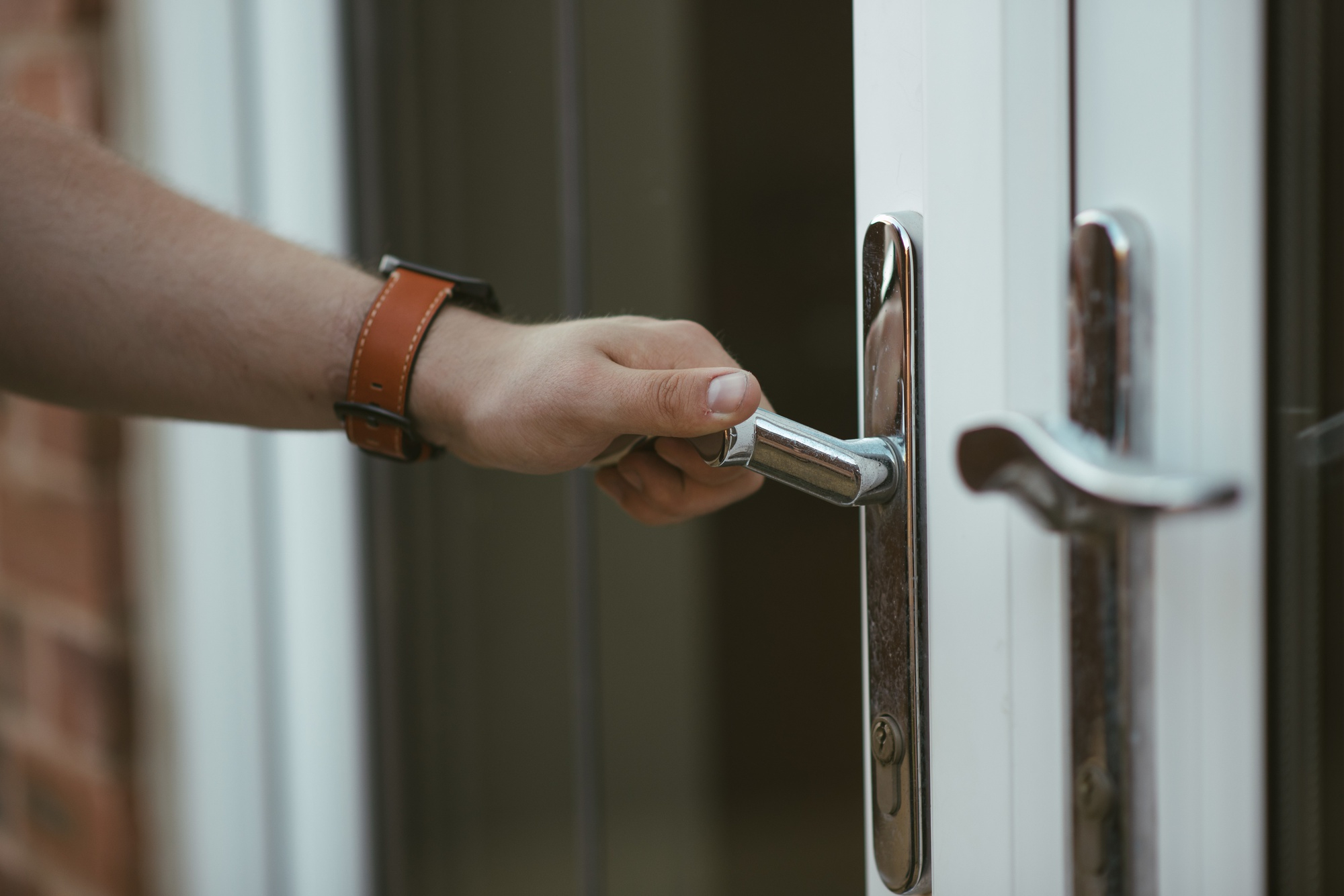 A hand trying to open a closed door holding its handle and trying to twist it down