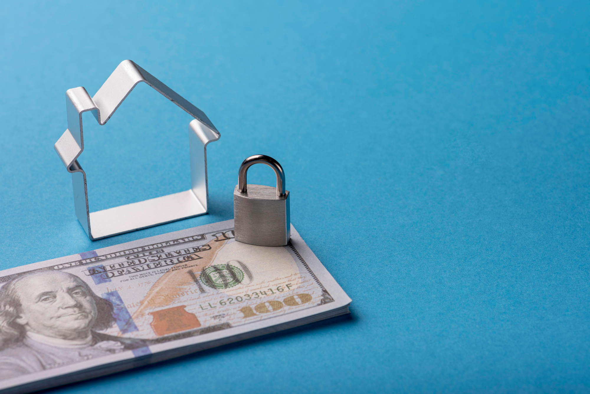 A scale model of a house sitting on a bunch of currency with a lock next to it