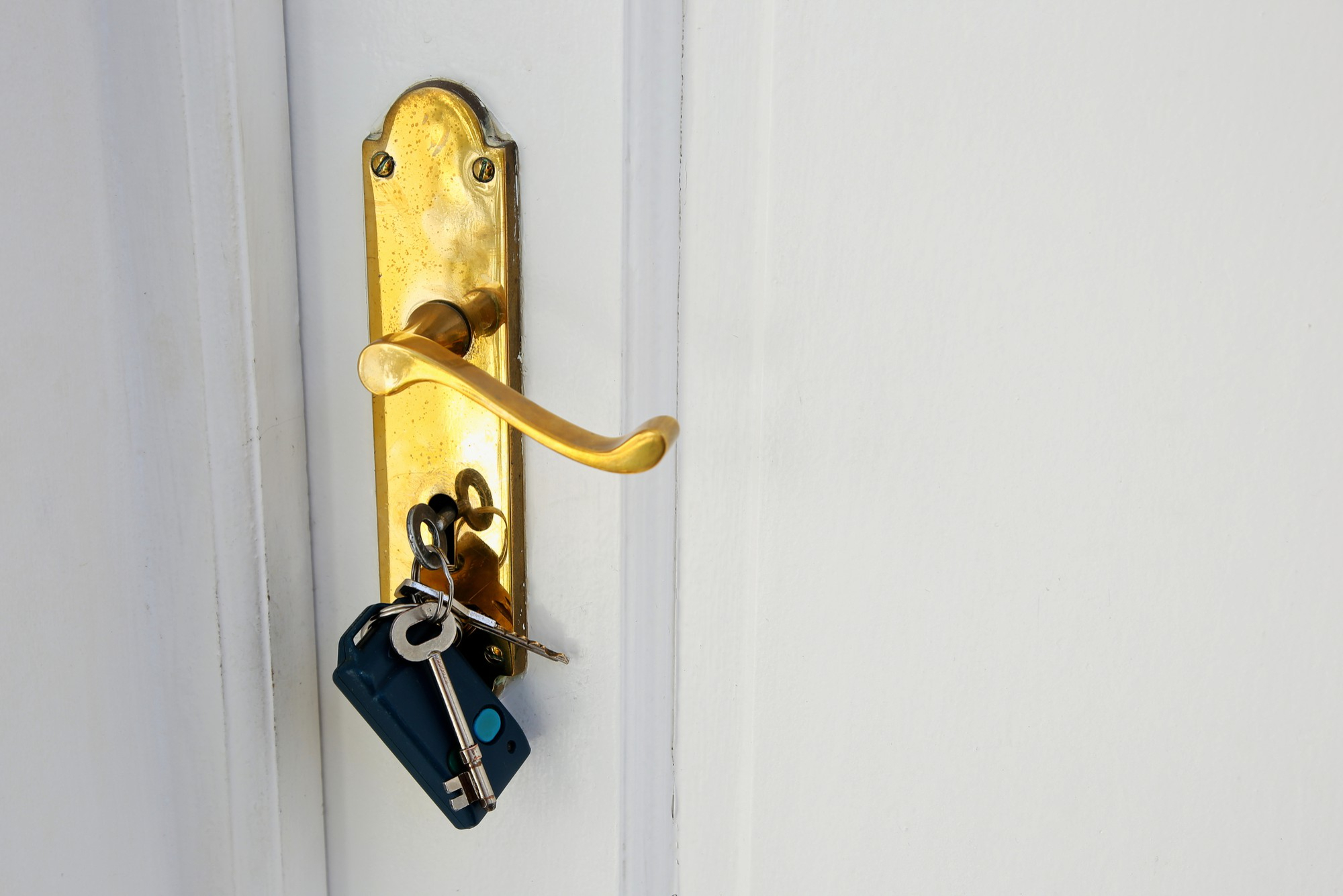 A golden-colored home lock with a set of House Keys hanging from it on a white door